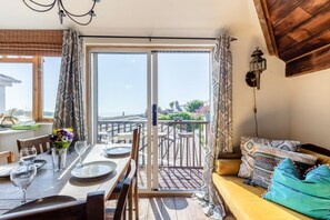 A dining area with a table set for two, a sofa with patterned cushions, and a balcony with a railing.