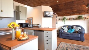 A kitchen with a wooden ceiling, a dining area with a sofa, and a TV mounted on the wall. - 3 Bed in East Prawle (oc-t30117) (East Prawle)