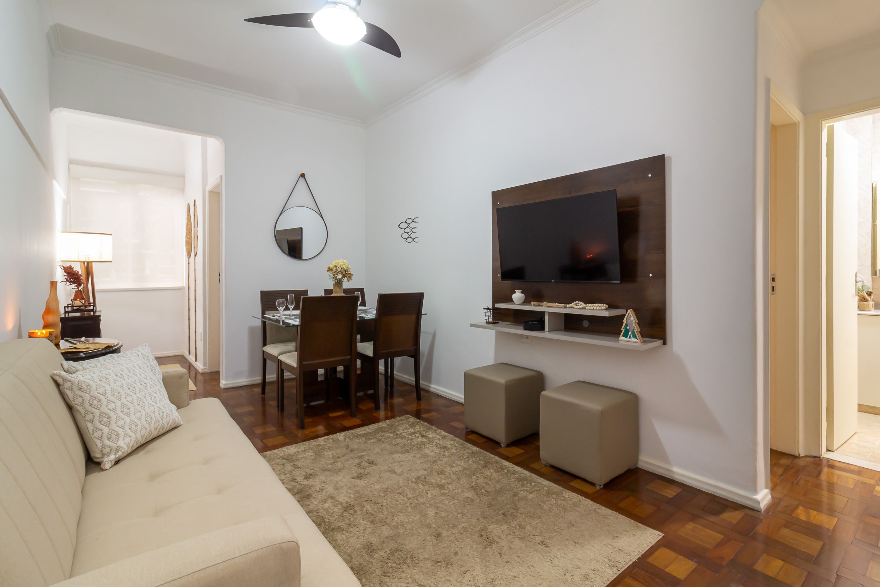 A living room with a sofa, a TV mounted on the wall, a dining table with chairs, and a small coffee table.