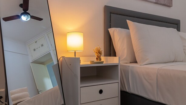 Ein Schlafzimmer mit Bett, Nachttisch, Lampe und einem großen Spiegel.
