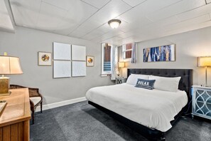 A bedroom with a large bed, a desk with a lamp, and artwork on the walls.