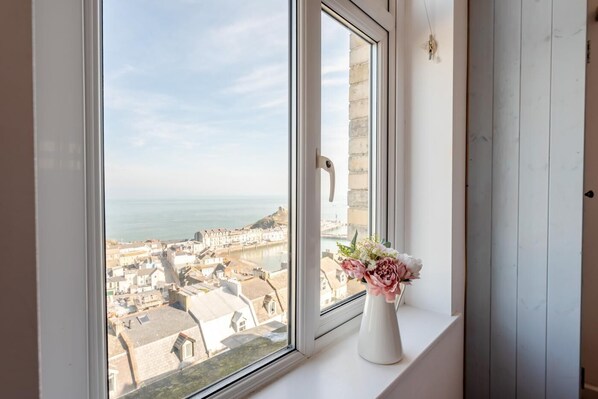 A window with a view of a coastal town, a white vase with flowers, and a door with a handle.