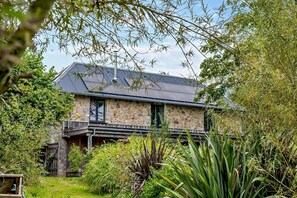 Une maison en pierre avec un toit sombre, entourée d’une végétation luxuriante et d’un jardin bien entretenu.