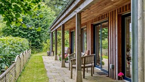 A covered outdoor area with stone flooring, wooden benches, and a view of a lush garden. - 3 Bed in Dartington (oc-b30033) (Dartington)
