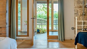 A room with a wooden wardrobe, a bed, and a view of a garden through a glass door. - 3 Bed in Dartington (oc-b30033) (Dartington)