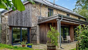 A rustic stone building with a wooden exterior, large sliding glass doors, and a covered patio area with outdoor seating. - 3 Bed in Dartington (oc-b30033) (Dartington)