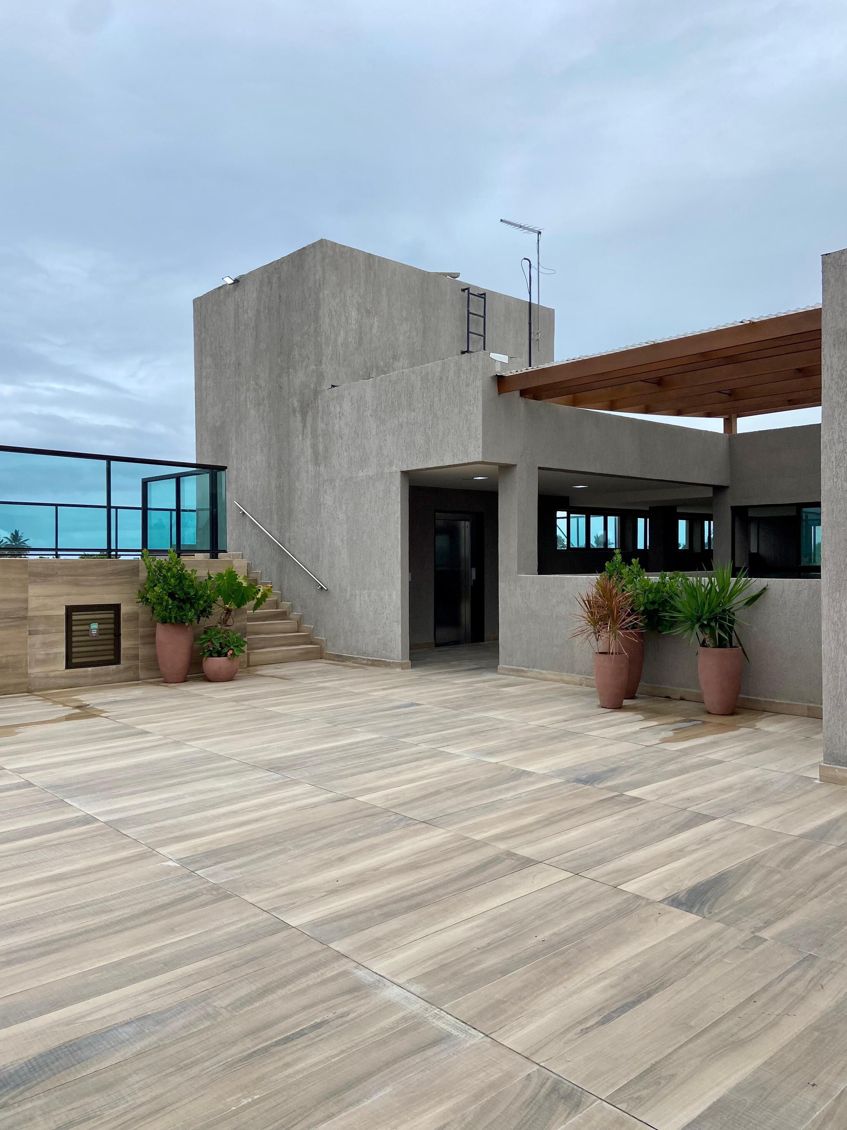 A modern building with a concrete facade, large windows, and a covered outdoor area with tiled flooring and potted plants.