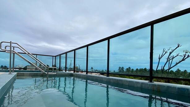 A swimming pool with a glass barrier and a metal staircase leading to a deck area. - Flat a 120 metros das Piscinas Naturais (Ipojuca)