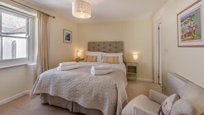 A neatly arranged bedroom with a large bed, bedside lamps, a chair, and a window with curtains.