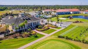 A golf course with a clubhouse, a pond, and a parking area.