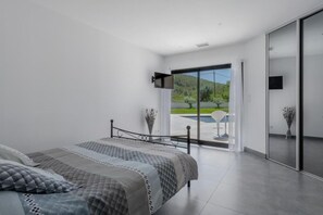 A modern bedroom with a large bed, a sliding glass door leading to a balcony, and a flat-screen TV mounted on the wall. - Villa with heated swimming pool, spa, gym and cinema (Cuges-les-Pins)