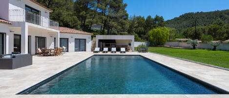 Una casa moderna con piscina, mobiliario exterior y vistas a árboles y colinas.