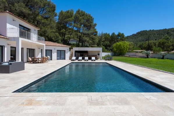 A modern house with a swimming pool, outdoor seating, and a view of trees and hills. - Villa with heated swimming pool, spa, gym and cinema (Cuges-les-Pins)