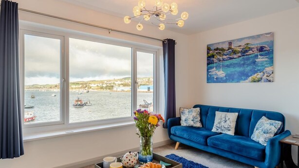A living room with a large window overlooking a harbor, a blue sofa, and a painting of a harbor scene.