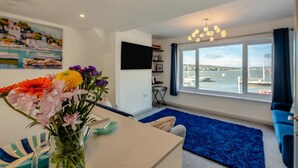 A modern living room with a large window overlooking a marina, a blue rug, and a vase of flowers on a table.