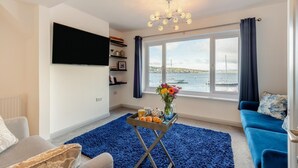 A living room with a large window, a flat-screen TV, a blue sofa, and a coffee table with a vase of flowers.