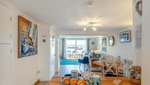 A cozy living room with a dining area, a painting of a boat on the wall, and a view of the sea through the glass door.
