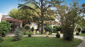 A garden with a large tree, a gazebo, and a building with a tiled roof. - Luxury Suite, terrace, private pool and jacuzzi (Noves)