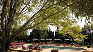 A poolside area with lounge chairs and umbrellas, surrounded by trees. - Luxury Suite, terrace, private pool and jacuzzi (Noves)