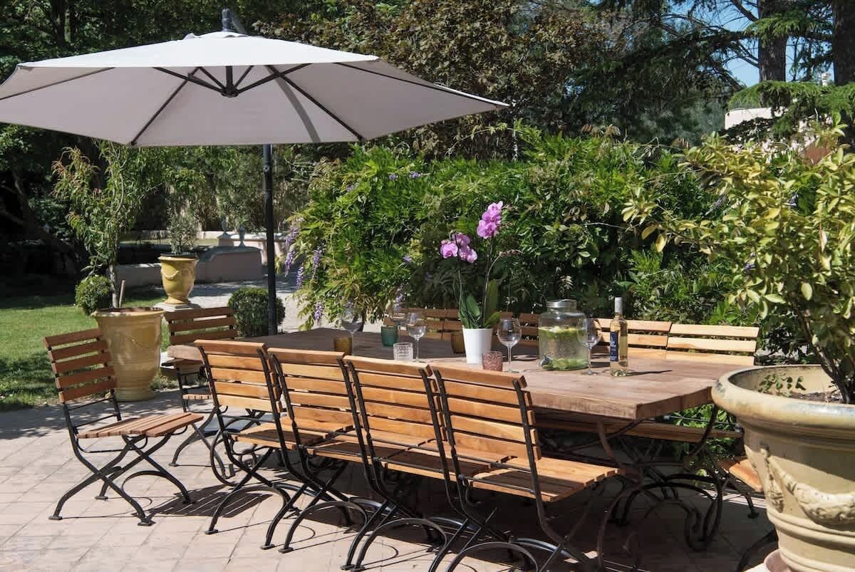 Une terrasse extérieure avec une table en bois, des chaises en métal, un grand parasol et des plantes en pot.