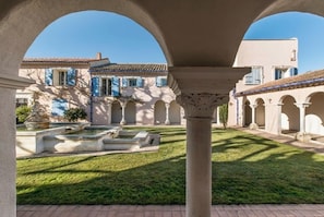 A courtyard with a fountain, arches, and a building with blue shutters. - Luxury suite with terrace and private pool and spa (Noves)