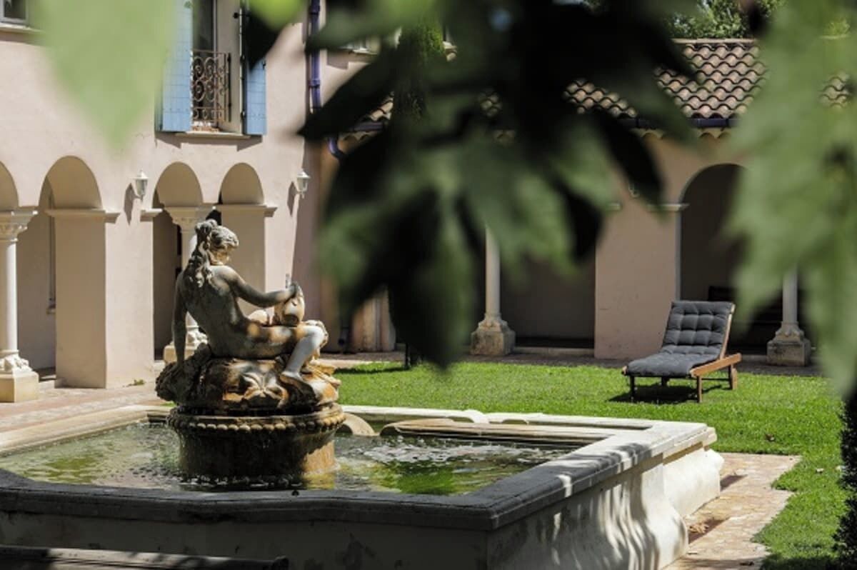Ein Innenhof mit Statue, Brunnen und Liegestuhl.