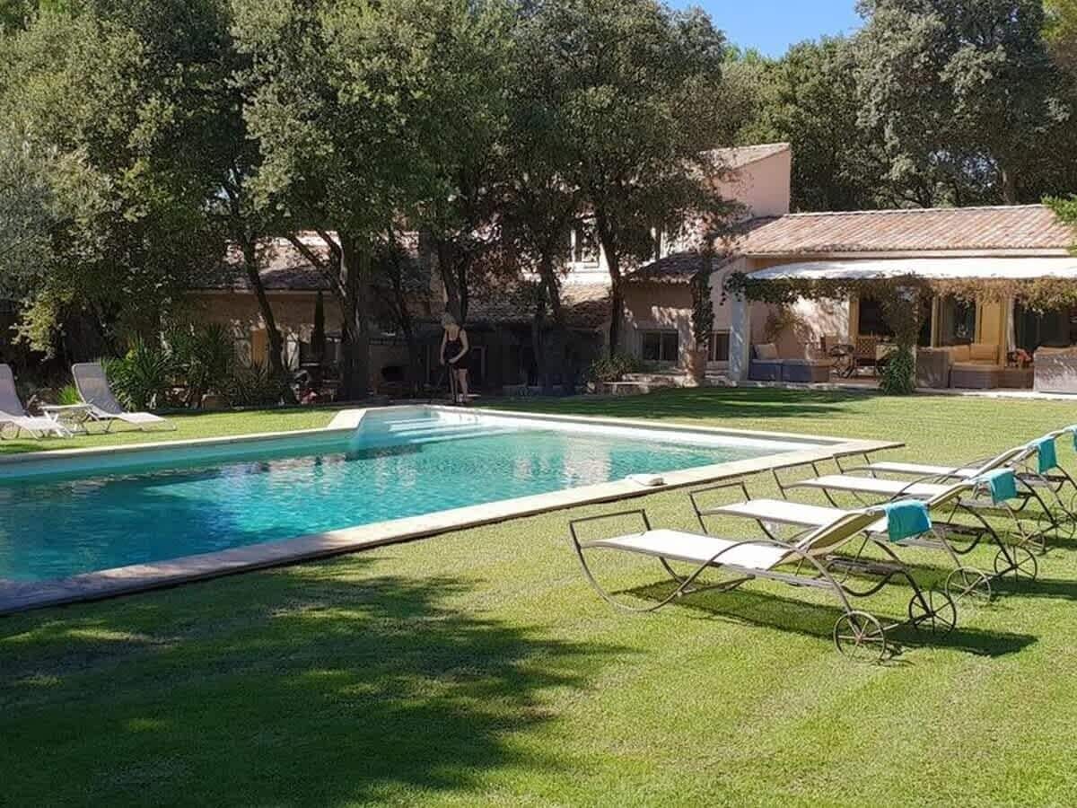 Ein rechteckiger Swimmingpool mit einer gefliesten Terrasse, umgeben von einem gepflegten Rasen und Bäumen.