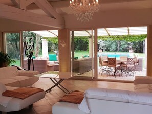 Un vaste espace de vie avec une grande porte-fenêtre coulissante donnant sur une terrasse aménagée avec du mobilier d’extérieur et une piscine.