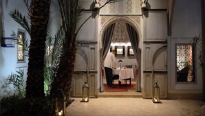 An ornate entrance with a table set for two, a palm tree, and lanterns. - Sublime suite at Riad Douceur with oriental decor (Marrakesh)