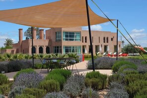 A modern building with a flat roof, large windows, and a patio area with outdoor seating. - Villa Sylana 2 Pools Tennis Court Hammam (Marrakesh)