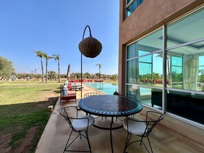 Eine Terrasse mit rundem Tisch und Stühlen, mit Blick auf ein Schwimmbad und einen angelegten Garten.