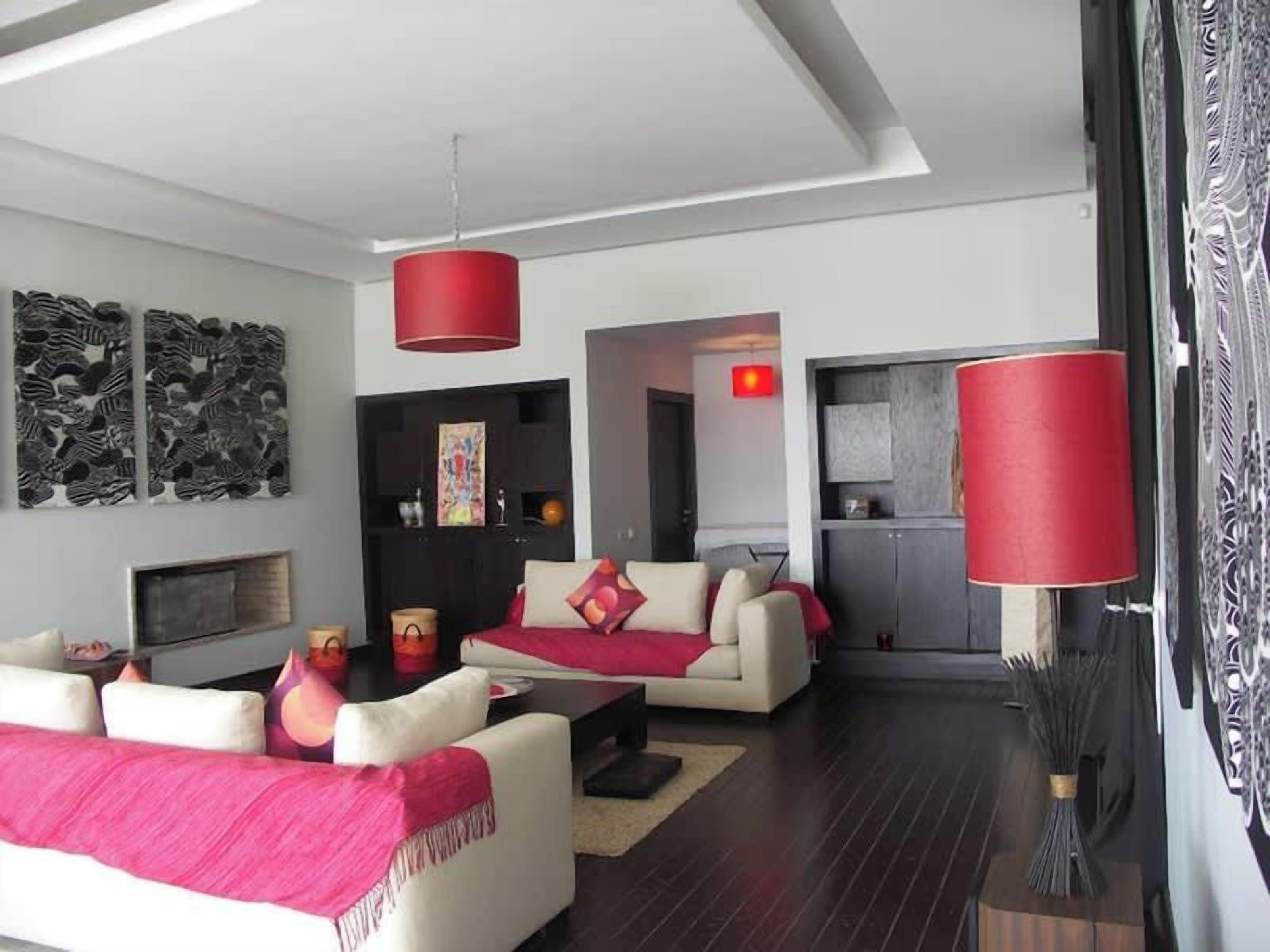 Un salon moderne avec un canapé, une table basse et des lampes rouges. On y trouve une cheminée et des œuvres d’art accrochées au mur.