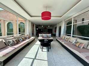 A spacious living area with a long sofa, a round table, and a red hanging light fixture. - Villa Sylana 2 Pools Tennis Court Hammam (Marrakesh)
