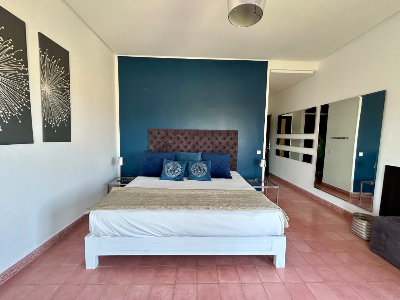 A bedroom with a bed, a headboard, a nightstand, a mirror, and a wall with artwork.