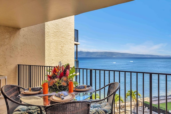 A balcony with a table set for dining, overlooking a body of water.