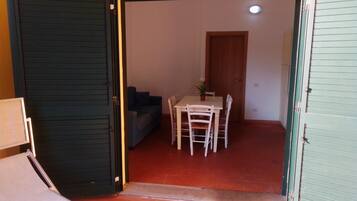 Eine offene Tür führt in einen Raum mit Esstisch, Stühlen, einer kleinen Couch und einer Topfpflanze.