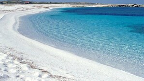 A beach with clear blue water, white sand, and a rocky shoreline.