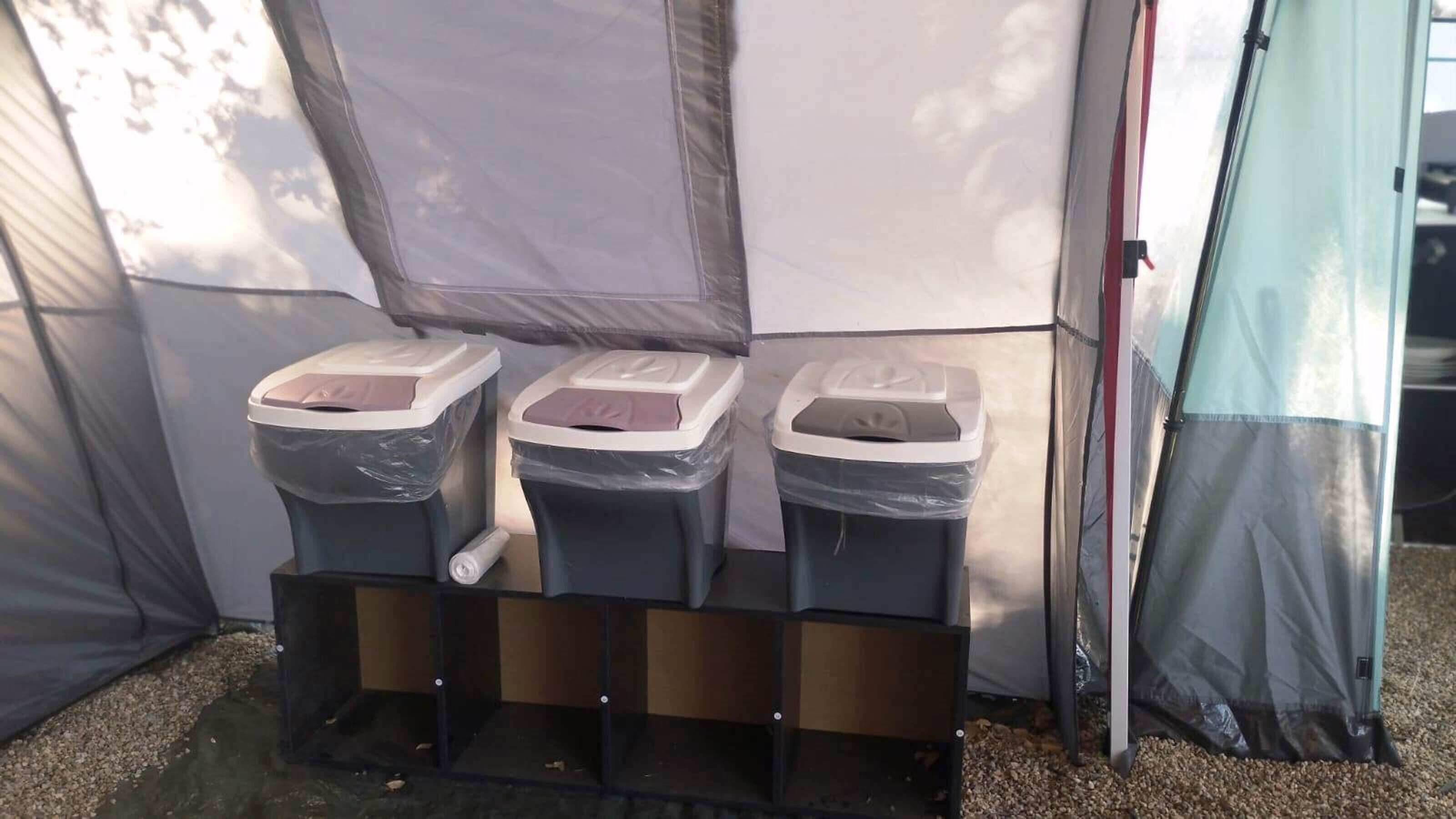 Un ensemble de toilettes portables comprenant trois poubelles, un réservoir d’eau et un écran de protection pour assurer l’intimité.