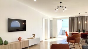 Un salon moderne doté d’un téléviseur à écran plat, d’un coin repas avec une table et des chaises, et offrant une vue sur l’extérieur.