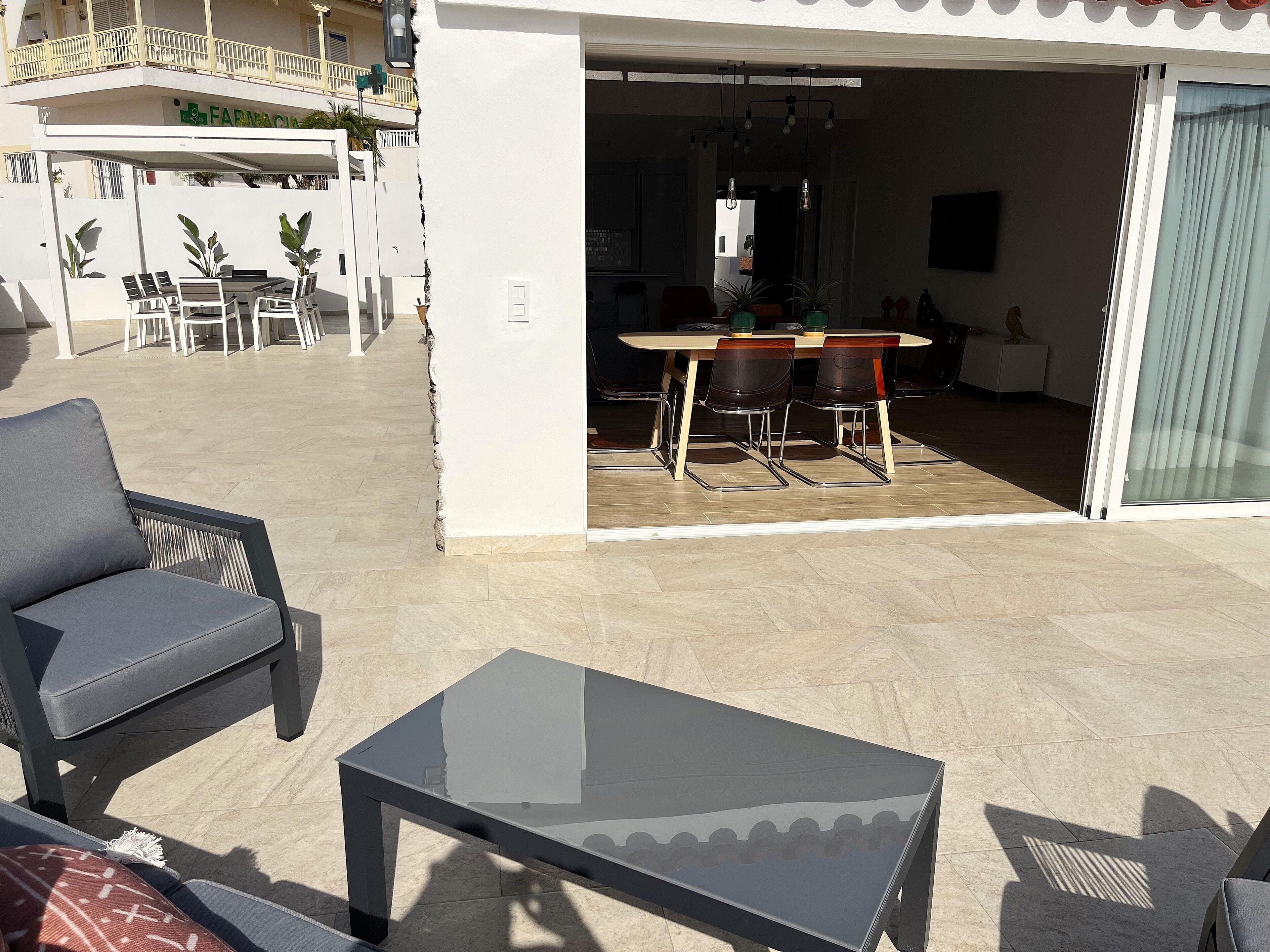 Un patio al aire libre con una mesa de vidrio, una silla acolchada y una mesa de comedor con sillas.