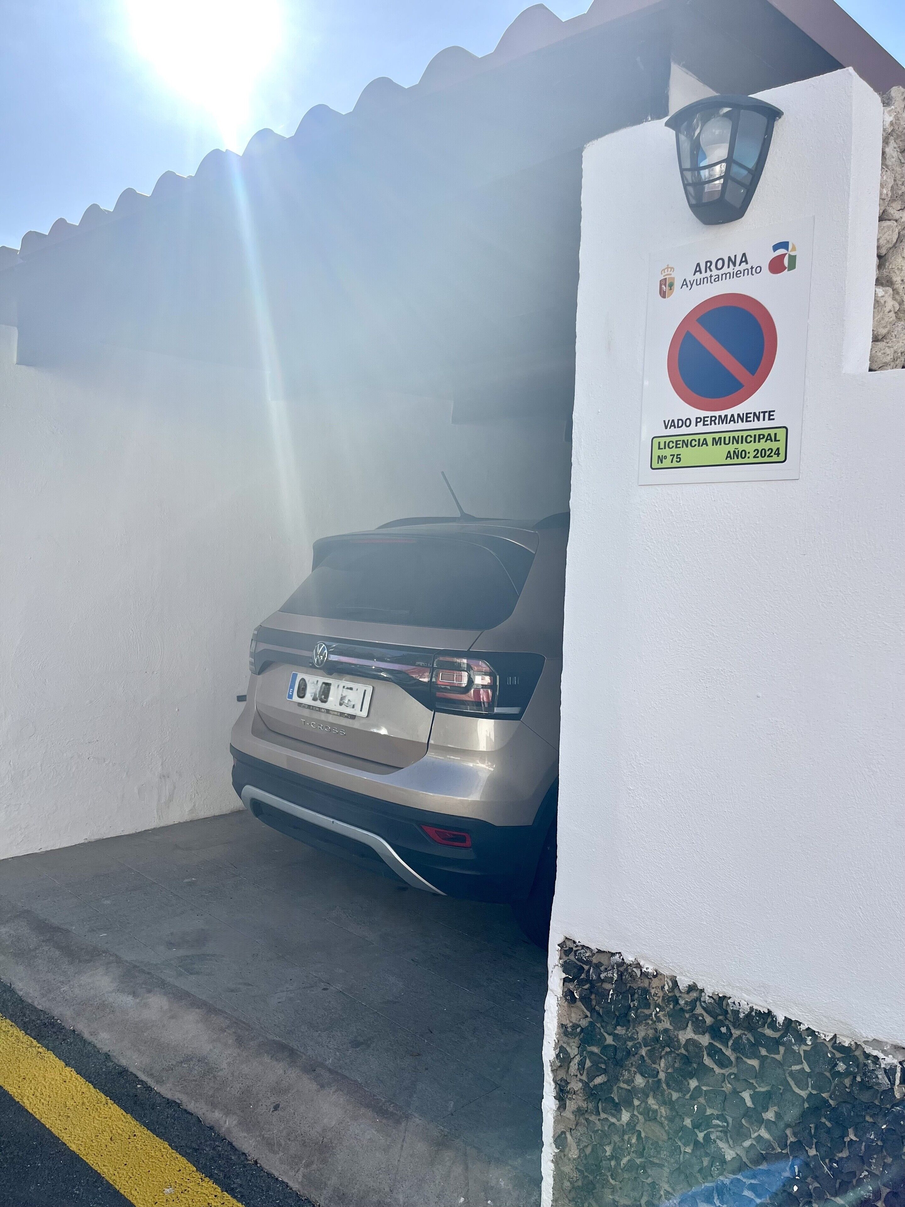 A parked car in a parking area with a no parking sign and a building with a light fixture.