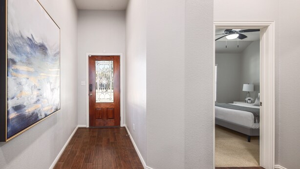 Un pasillo con una puerta de madera, un cuadro en la pared y una habitación visible a través de una puerta abierta.