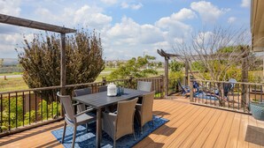 Una terraza de madera con mesa y sillas, rodeada por una pérgola de madera y vista a una zona residencial.