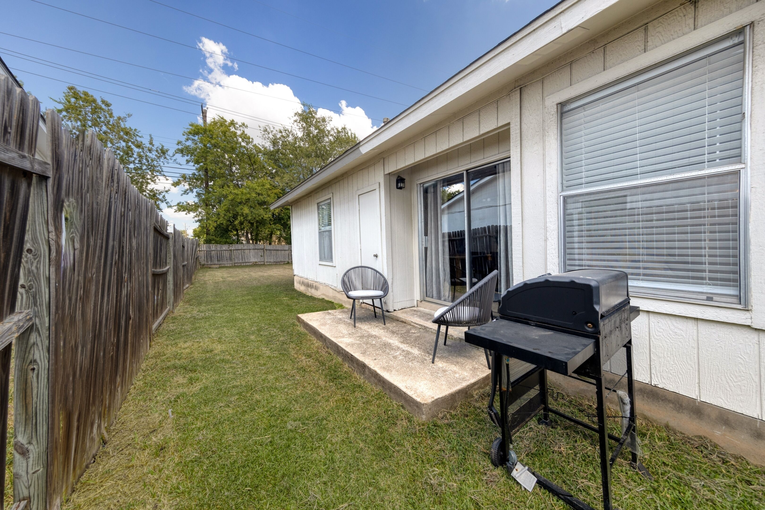A residential backyard with a patio, a grill, and a wooden fence.