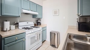 Een keuken met blauwgroene kastjes, een witte kookplaat, een roestvrijstalen spoelbak en een prullenbak.