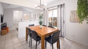 Een eetgedeelte met een houten tafel en stoelen, een keuken op de achtergrond en een schuifdeur naar een balkon.