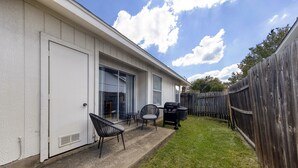 Een woonhuis met een garage, een overdekt terras met tuinmeubilair en een houten omheining.