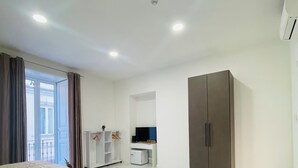 Ett modernt hotellrum med en säng, en soffa, en garderob, en TV och ett litet pentry.
