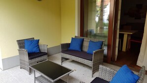 A patio area with wicker furniture, including two sofas and a coffee table, against a yellow wall. - Apartment Near Romerbad Thermal Spa (Bad Kleinkirchheim)