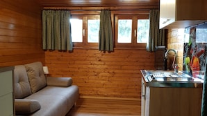 A cabin interior with a sofa, wooden walls, a kitchen area, and windows with curtains. - Apartment Near Romerbad Thermal Spa (Bad Kleinkirchheim)